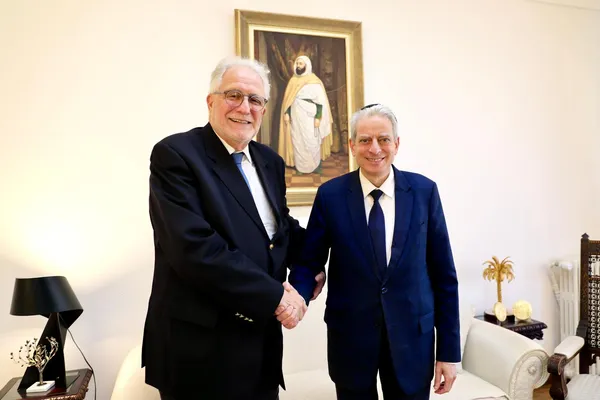 Chems-Eddine Hafiz, Rector of the Grand Mosque of Paris, and Chief Rabbi Moshe Lewin shaking hands and smiling, in front of a portrait painting.