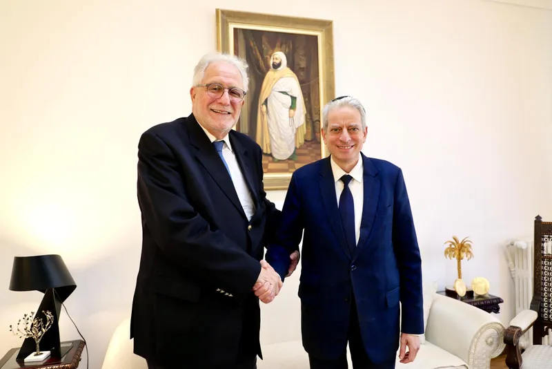 Chems-Eddine Hafiz, Rector of the Grand Mosque of Paris, and Chief Rabbi Moshe Lewin shaking hands and smiling, in front of a portrait painting.