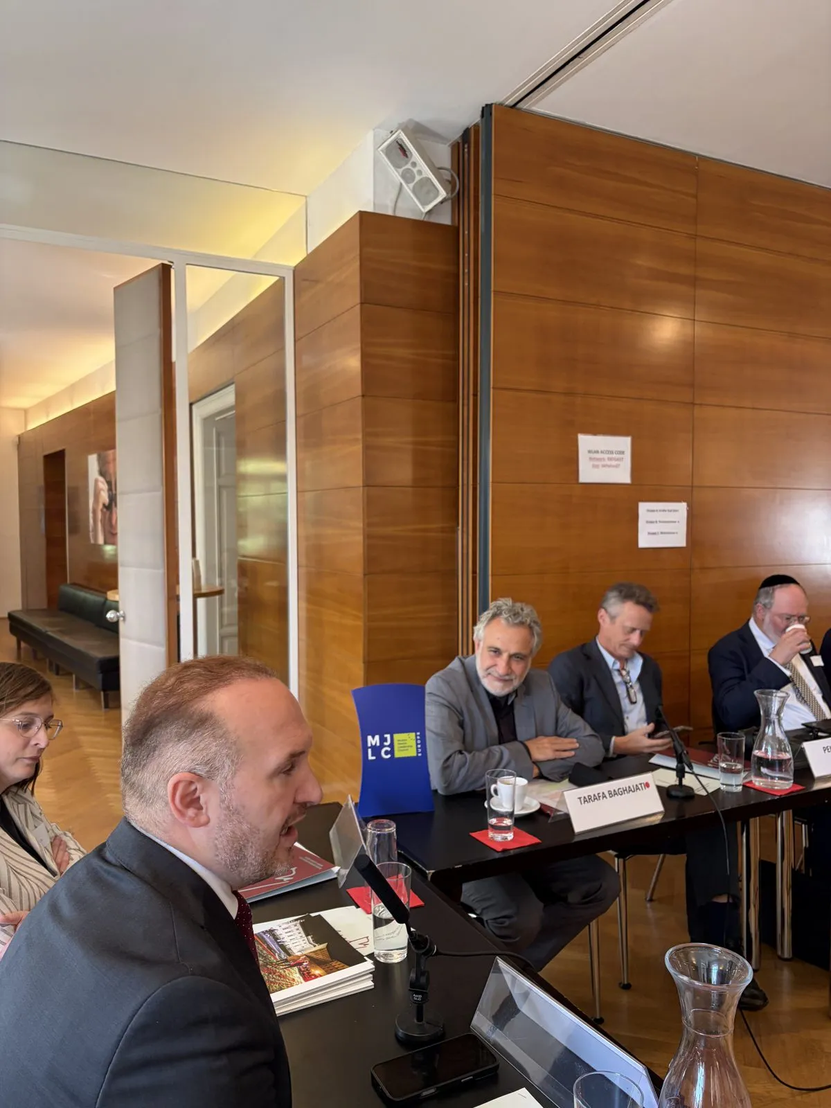 A participant speaking in the foreground during the workshop, with the MJLC roll-up banner behind the table.