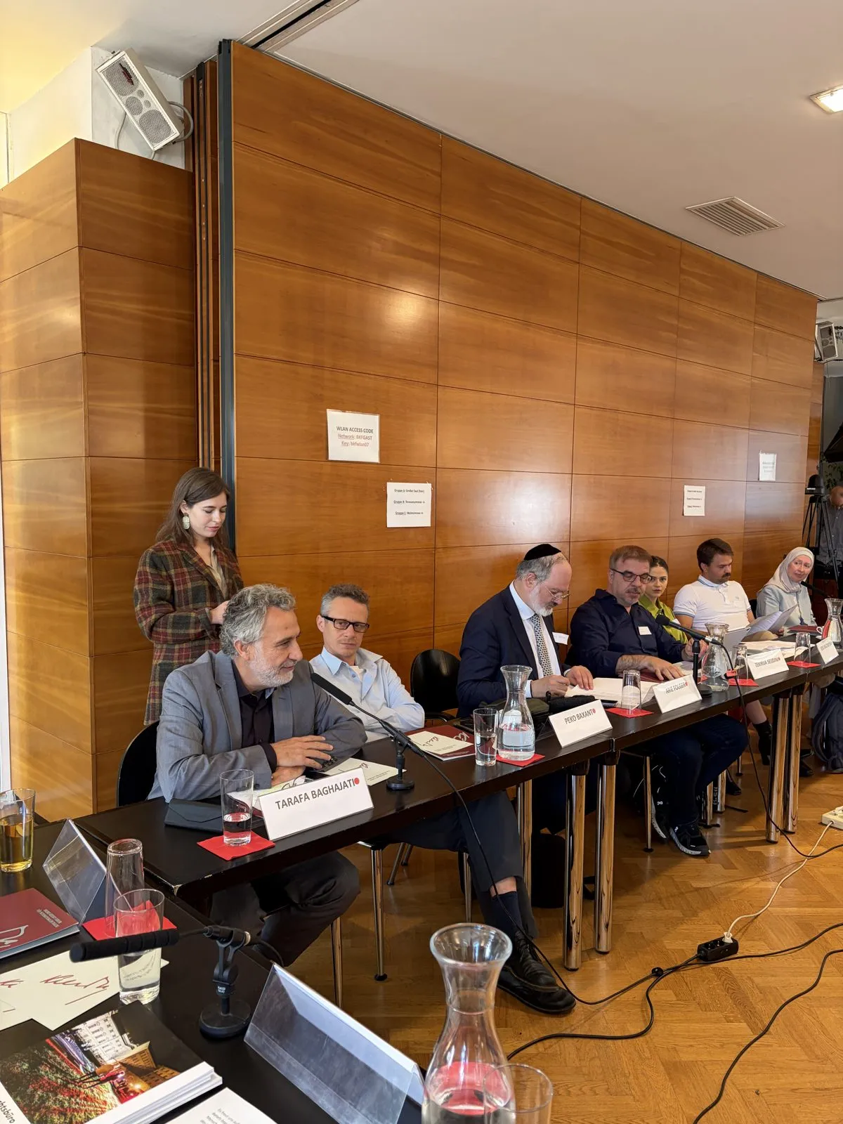 Imam Tarafa Baghajati speaking at the workshop table, with other participants seated alongside.